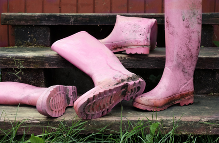 Abandoned dirty pink rubber boots on the wooden stairs. Outdoor cropped photoの写真素材