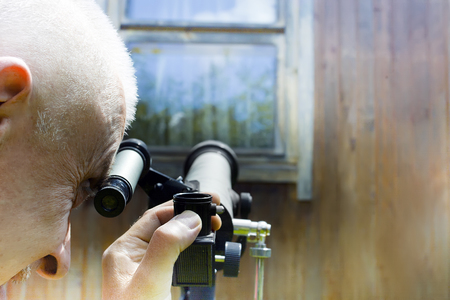 Filtered photo of a man spying at telescope, a window in the background outdoor cropped shotの写真素材