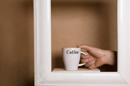 Human hand in painting frame holding a mug with coffee, cropped studio shotの写真素材