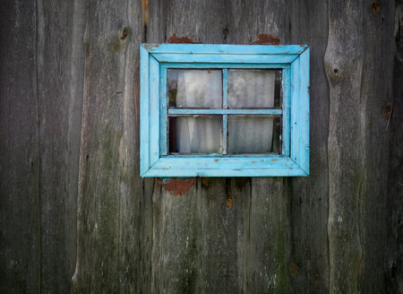 Abandoned wooden house wall with a window frame painted in blue, outdoor cropped photo
