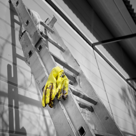Yellow rubber gloves laid on the telescopic ladder next to the fresh painted wall of a wooden house, selective color square shotの写真素材