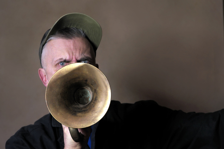 A man with aggressive look playing old horn, focus in the foreground. Studio portraitの写真素材
