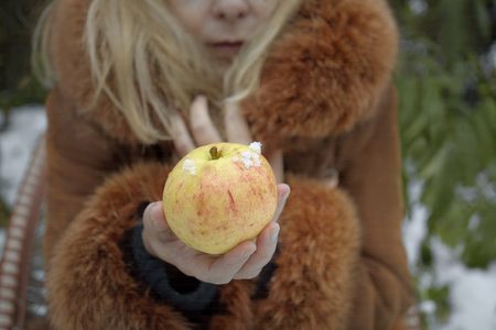 Woman wearing fur coat holding apple, a winter landscape in the backgroundの写真素材