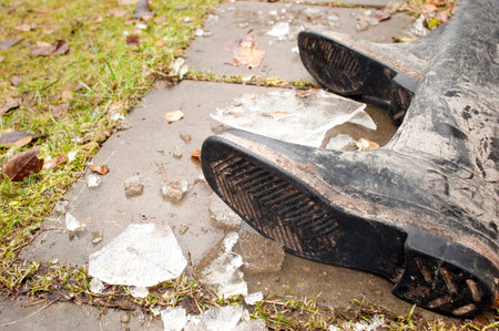 Human legs wearing dirty rubber boots laid across the foot path covered with ice, outdoor cropped shotの写真素材