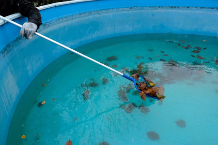 A worker hands with leaf net cleaning a residential swimming pool