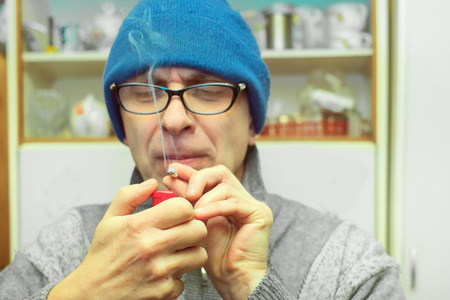 Man wearing glasses lighting a joint or cigarette in the kitchen, indoor filtered shotの写真素材