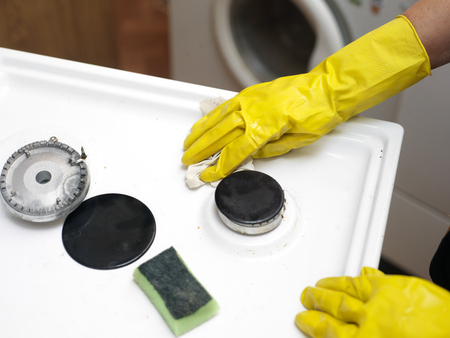 Female hands wearing protective gloves cleaning a gas stove topの写真素材