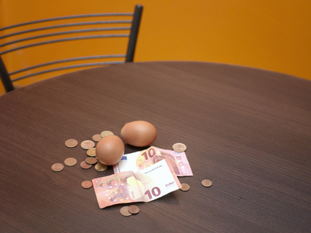 Banknotes and coins spread out on the table top next to a couple of eggs, concept of food expensesの写真素材