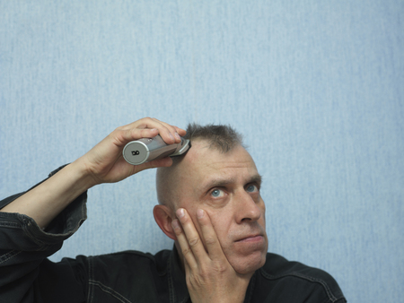 Portrait of a man cutting his hair with electric hair trimmerの写真素材
