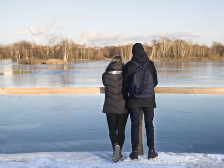 Romantic looking couple standing on a pier, a winter landscaspe with frozen river in the backgroundの写真素材