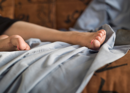 Bare female legs with pedicure laid on unmade bed or sofa, indoor cropped shotの写真素材