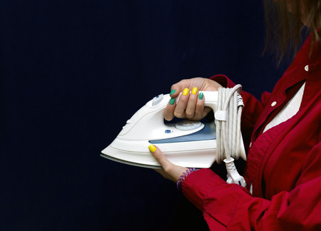 Female hands with manicured nails holding electric iron, cropped studio shotの写真素材