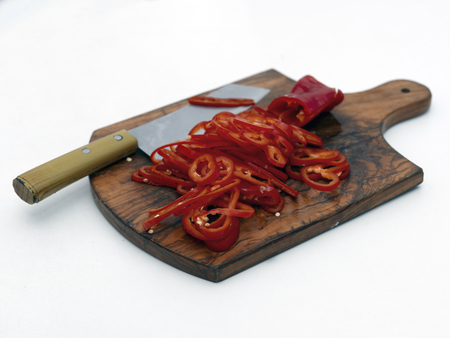 Sliced pepper and kitchen knife on the wooden chopping board laid on a white table topの写真素材
