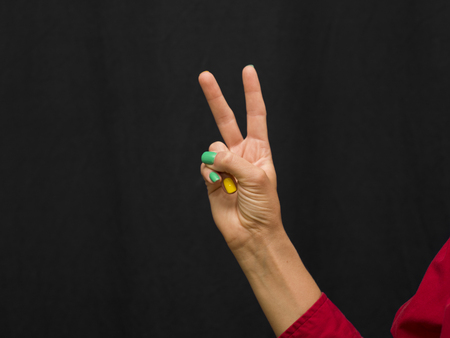 Woman with manicured nails hand gesturing victory sign, studio closeupの写真素材