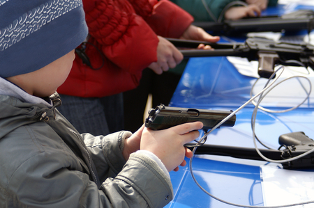A kid holding a gun tethered with metal cable in a shooting galleryの写真素材