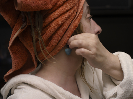 A woman with a bath towel on a hand putting earrings, indoor closeupの写真素材