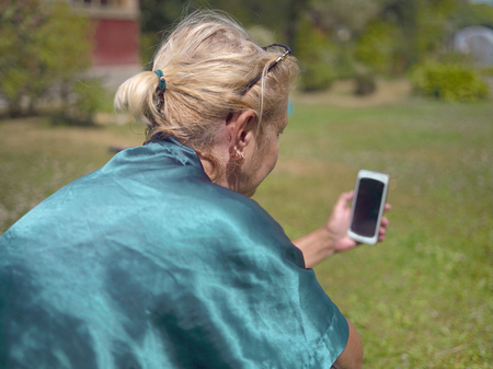 A woman sitting outdoors with mobile phone in her handの写真素材