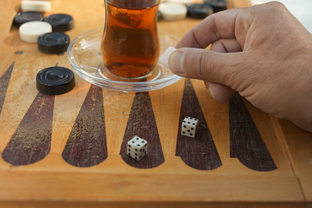 Hand adding sugar into a glass of traditional tea placed on a backgammon