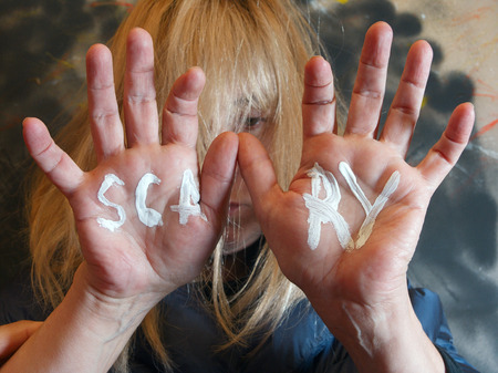 selective focus portrait of a woman with hands in front of her face and a word Scary written on themの写真素材