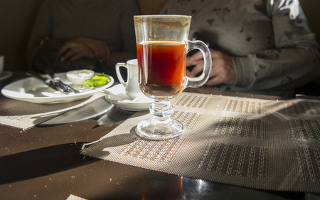 Cup of hot coffee on a messy table and two people in the background, indoor cropped shotの写真素材