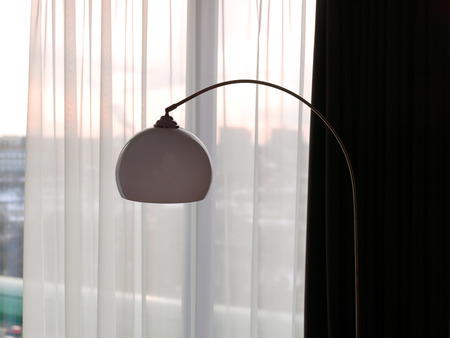 Cropped shot of a silhouette of a modern electric lamp against semi-transparent curtain and sunset sky in the backgroundの写真素材