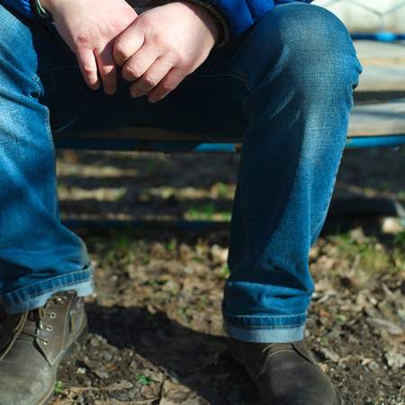 A man sitting outdoor with interlocking fingers, outdoor square shotの写真素材