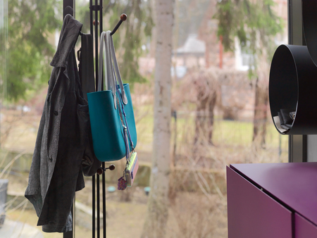 Modern hallway with handbags and clothes hanging on a metal hanger, interior shot with window in the...