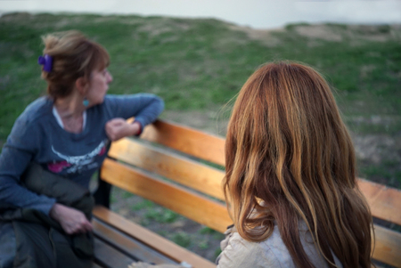Two women sitting on a bench, outdoor sunset light imageの写真素材