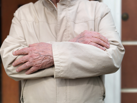 Senior man standing with hands crossed on his chest, outdoors close-upの写真素材