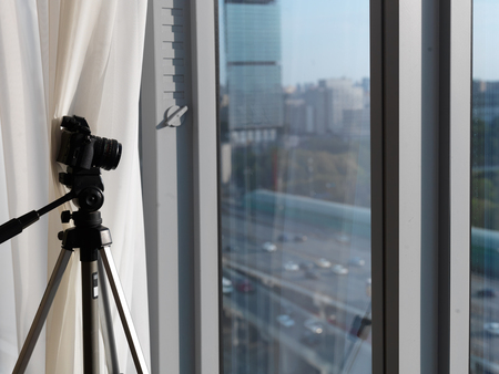A camera on a tripod pointed through the window, a blurred cityscape in the background
