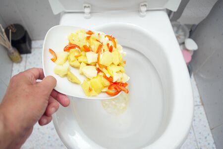 A hand throwing wasted food into a toilet, indoor close-up