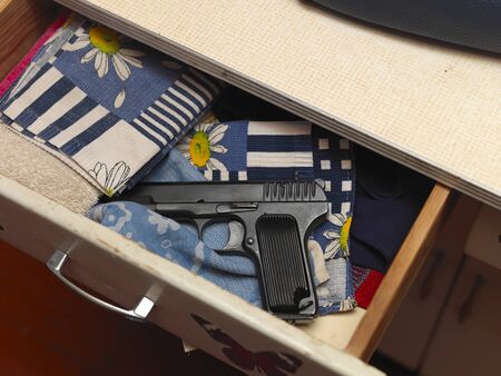 A handgun keeping in a cupboard drawer along with kitchen towels, indoor close-up,
