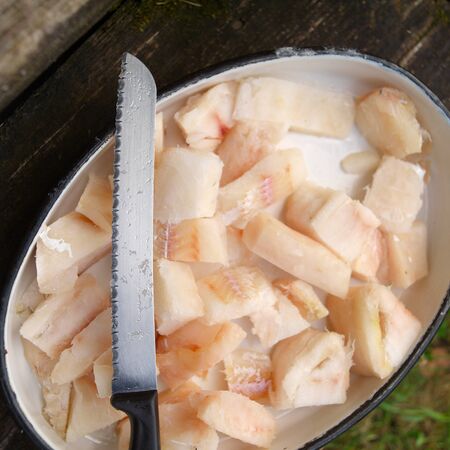 Close-up of a kitchen knife and sliced raw fish fillet in a food bowl