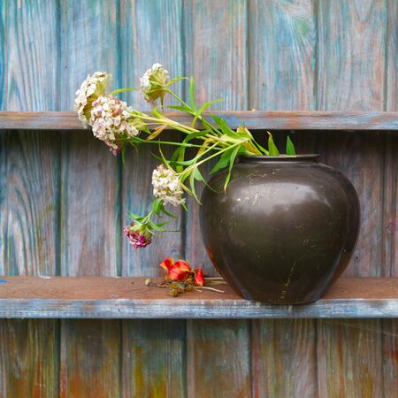 A vase with bouquet on a shelf against the wooden painted wall, outdoor still lifeの写真素材