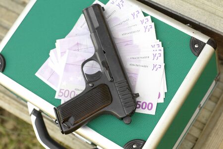 Heap of european currency and a handgun laid on the green briefcaseの写真素材