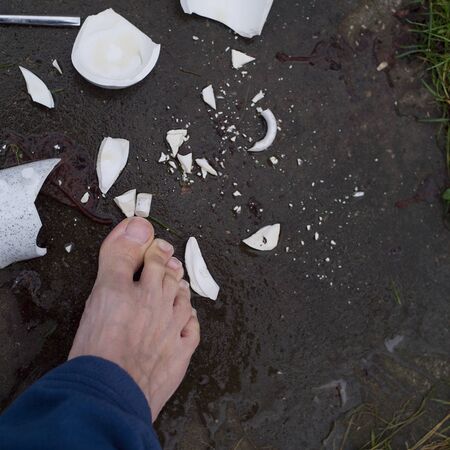 Broken tea cup and a bare foot about to step on it, outdoor close-upの写真素材
