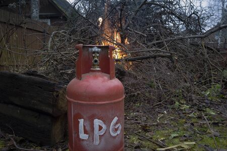 Red LPG bottle placed extremely close to burning firewood, outdoor shotの写真素材
