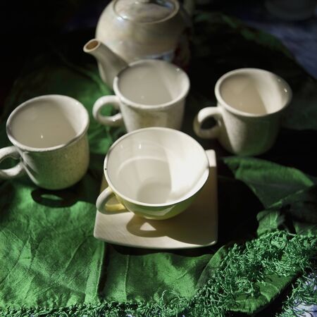 Tea pot and empty cups on a table covered with green cloth, foxus in the foregroundの写真素材