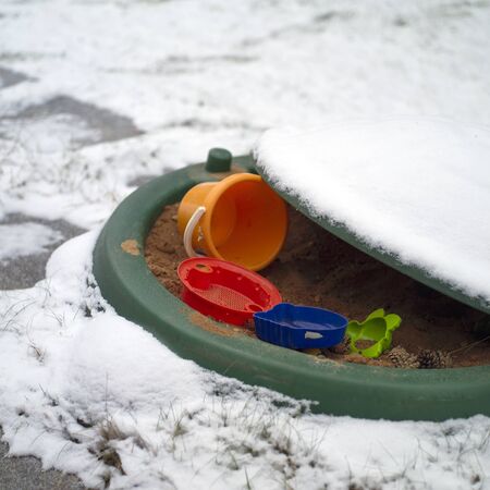 Abandoned toys in a sandbox, outdoor closeup, winter scene