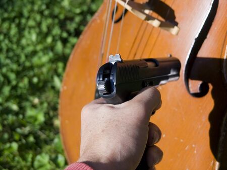 A hand wiith a gun pointing at cello, oudoor close-up