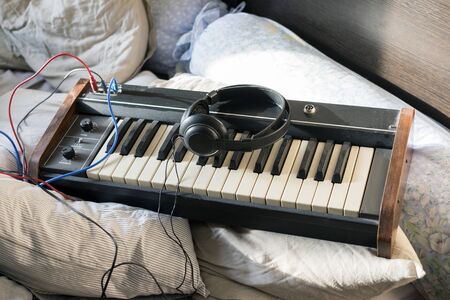 Headphones and synthesizer placed on unmade bed, concept of bedroom music studio