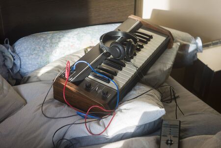 Synthesizer abandoned on a messy bed, concept of home music studio