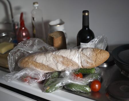 Food straight from a shop in plastic bags and a bottle of wine in a mess on electric stoveの写真素材