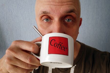 Indoor closeup portrait of a matured man with a straight look drinking coffeeの写真素材