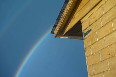 Part of a wooden house and rainbow in the backgroundの写真素材