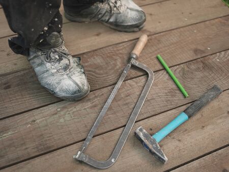 Hand tools dropped on wooden floor next to worker in dirty boots