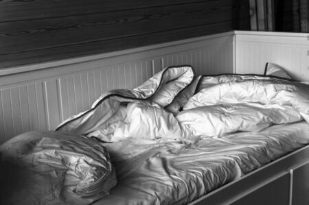 Unmade bed and crumpled bedding after a slepples night, in black and white