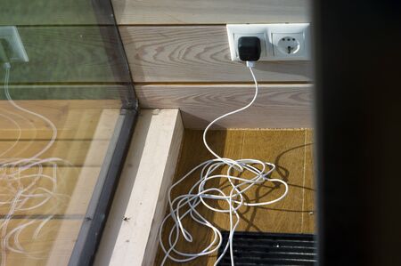 Tangled USB cable on the floor, plugged in electric socket, indoor closeup
