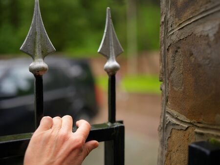 Hand opening a metal door with spear like top section, outdoor close-upの写真素材