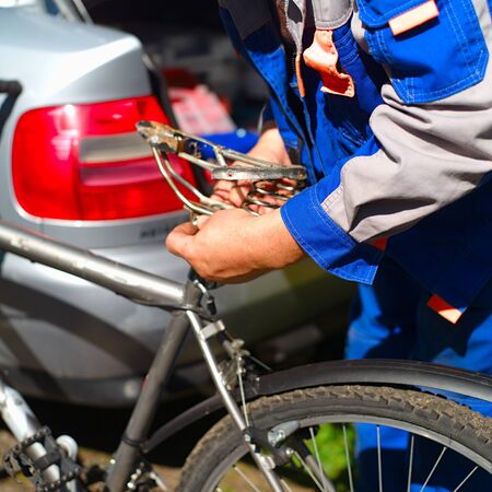 Hands of mechanic replacing a bicycle seat, an open car boot in the background